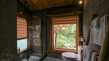 Un baño con techo de madera, inodoro, lavamanos y ventana con vistas a un jardín.