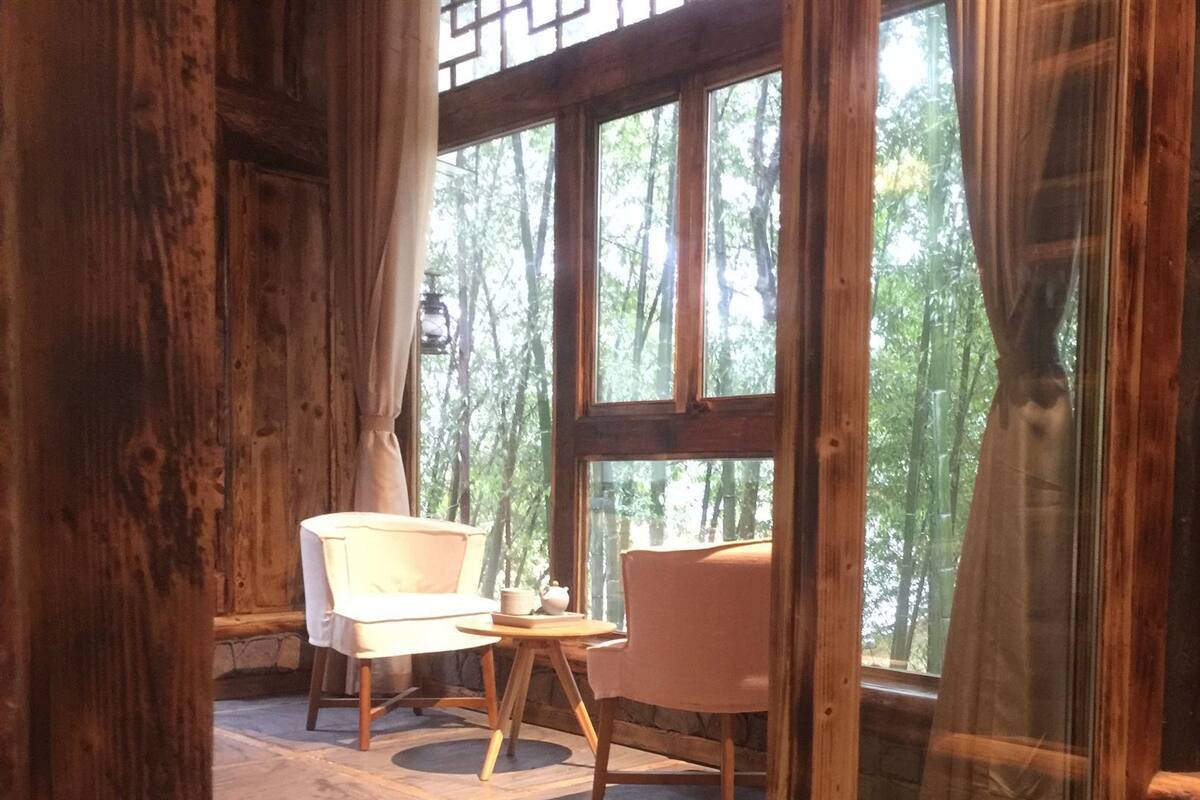 Een kamer met twee stoelen, een tafel en een groot raam met uitzicht op bomen.