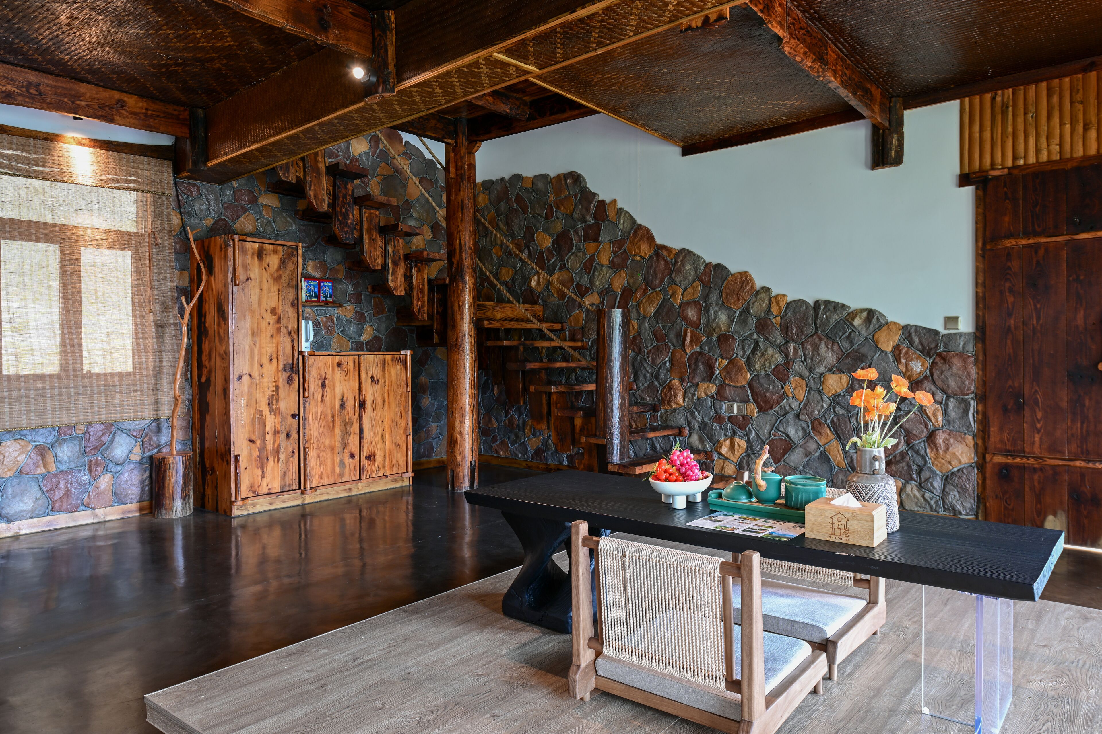 Ein geräumiger Raum mit einer Steinwand, einer Holztreppe und einem schwarzen Esstisch mit Stühlen.