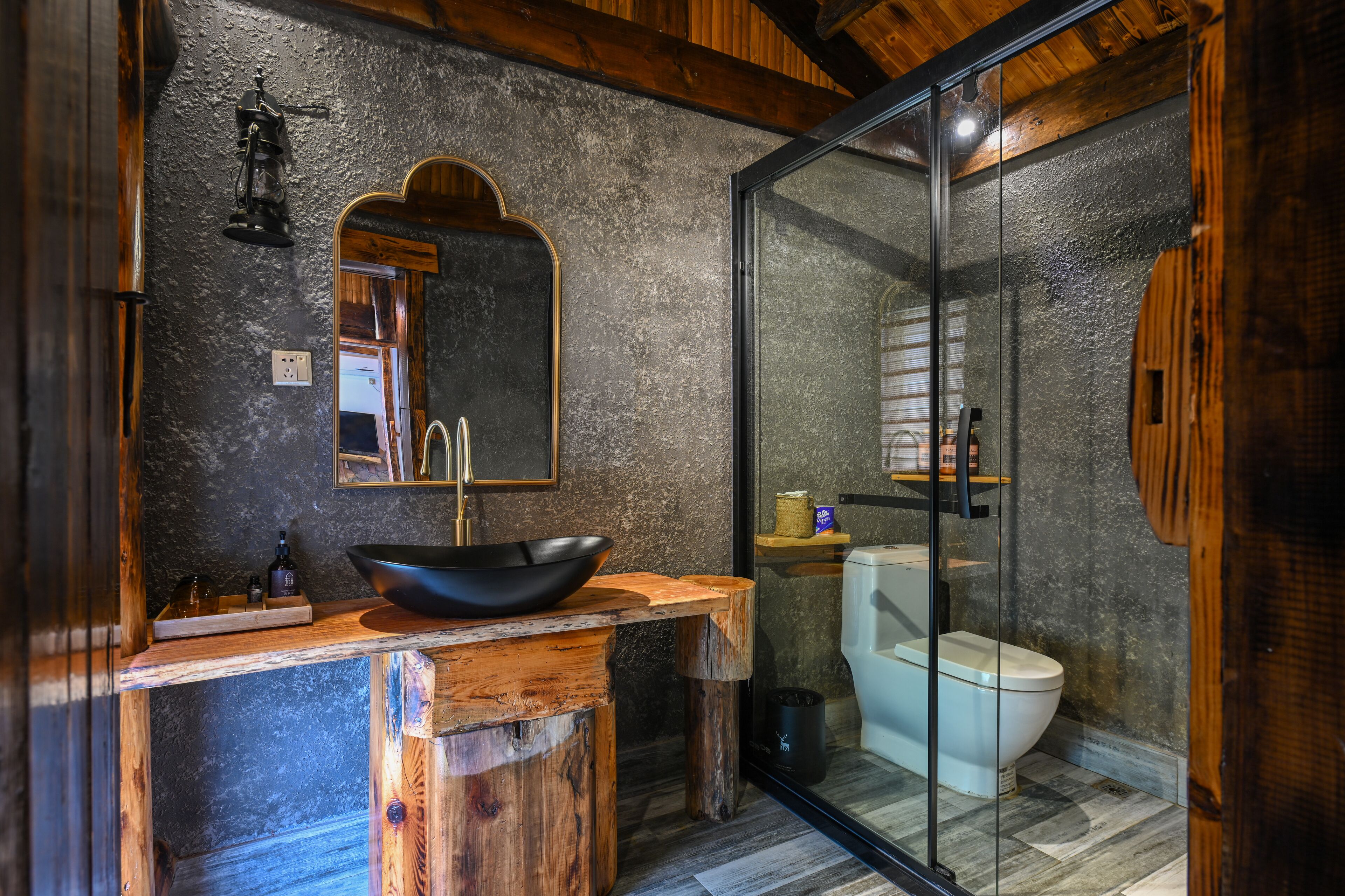 A rustic bathroom with a wooden vanity, a black basin, a mirror, and a glass-enclosed shower area.