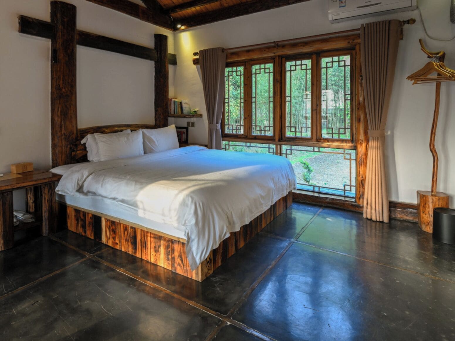 Un dormitorio con una cama grande, vigas de madera, un ventanal con cortinas y suelo de madera.