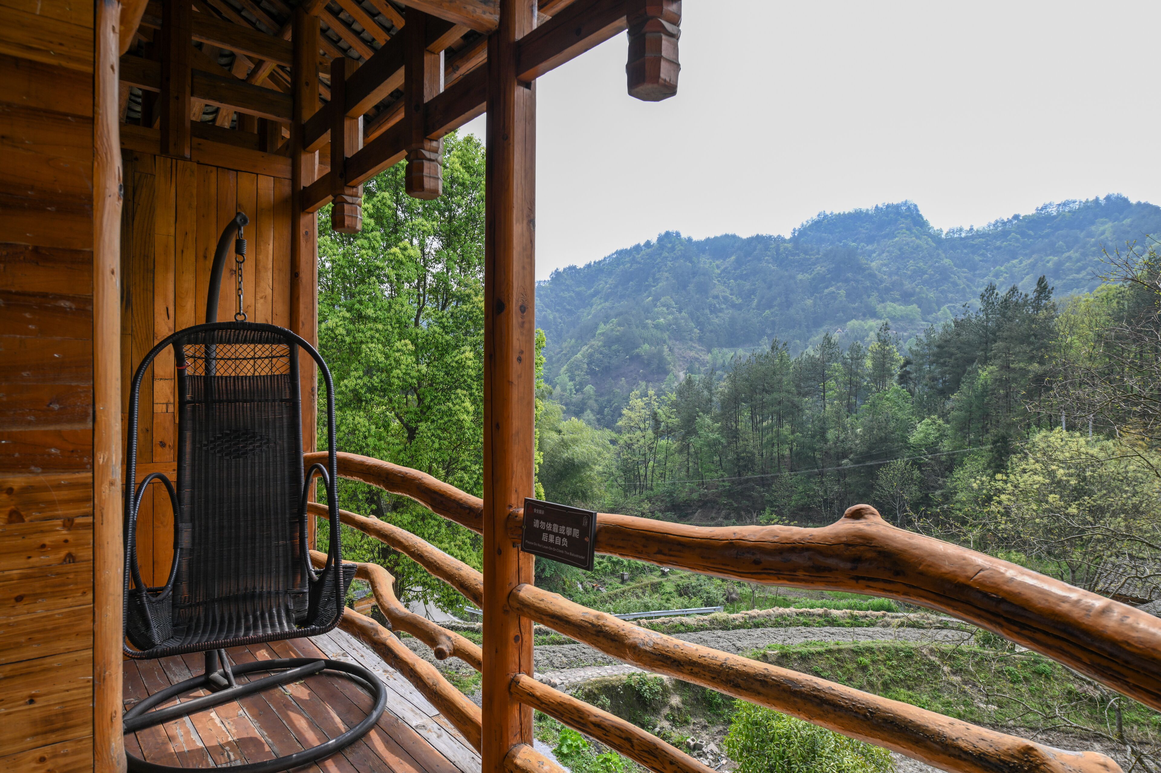 A wooden deck with a wicker chair and a wooden railing overlooking a forested valley.
