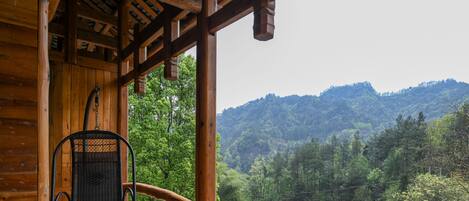 A wooden deck with a wicker chair and a wooden railing overlooking a forested valley.