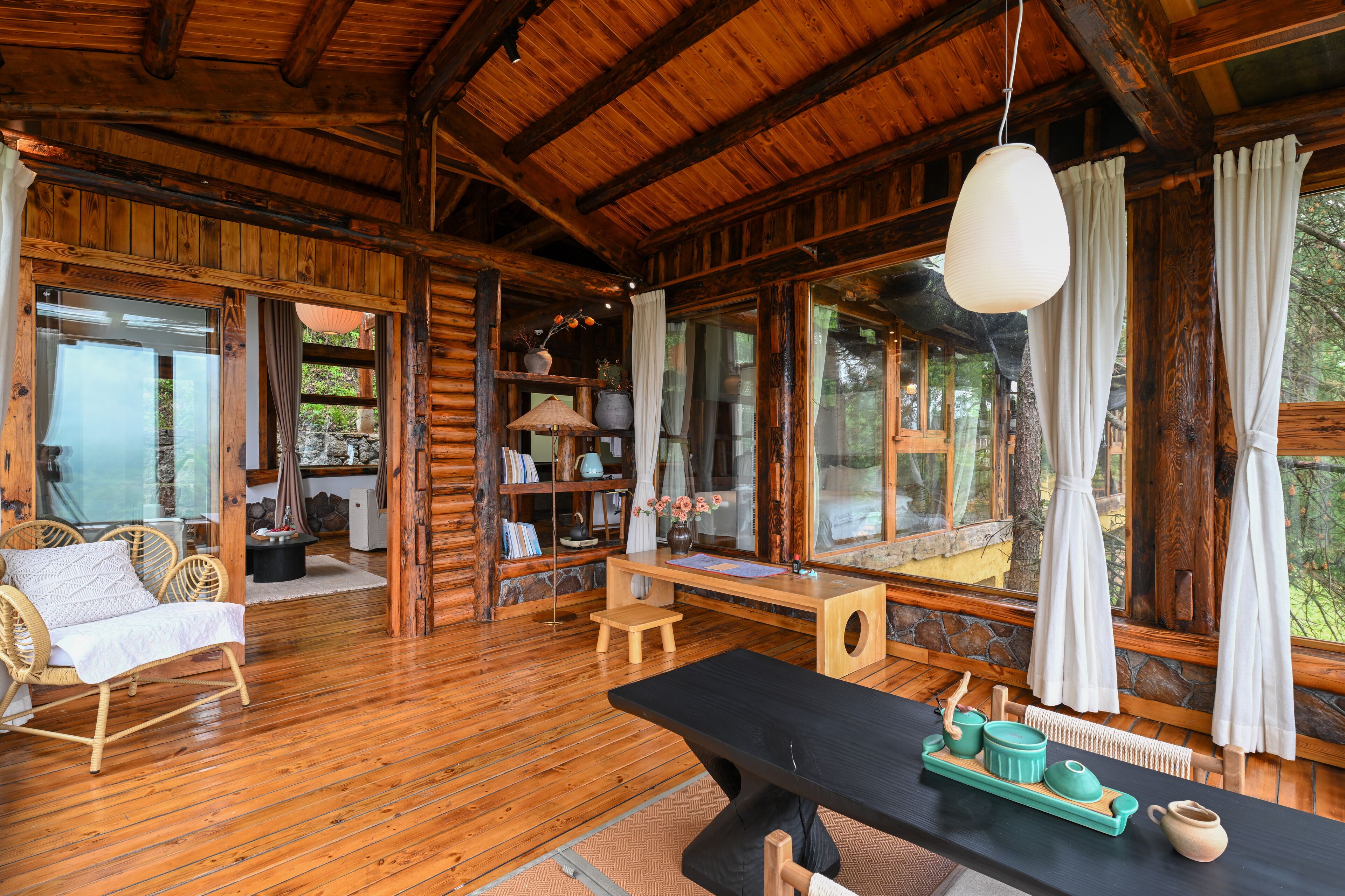 A wooden cabin interior with a dining table, chairs, and a bookshelf.