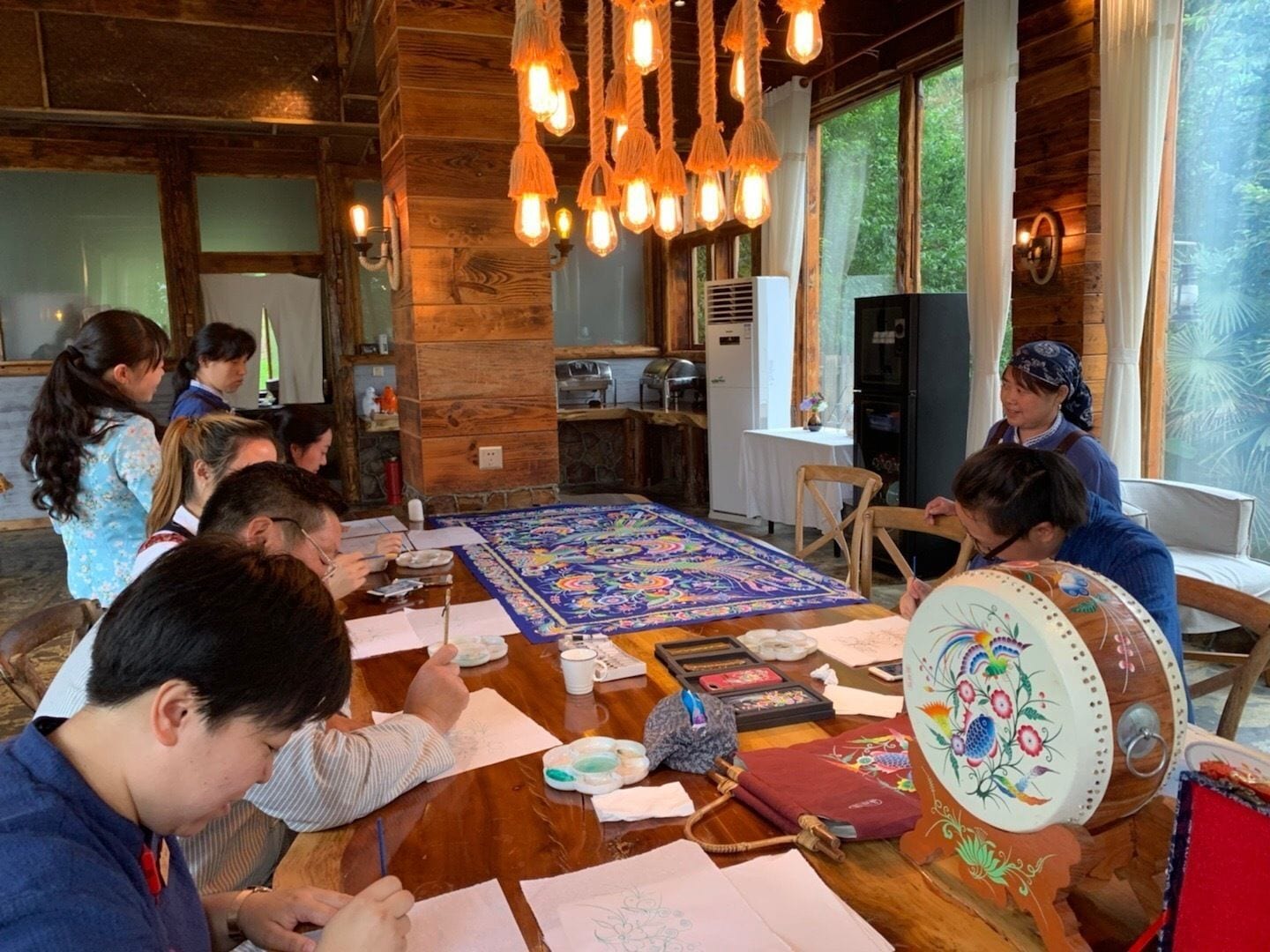 A group of people engaged in a painting activity in a rustic room with wooden walls and large windows.
