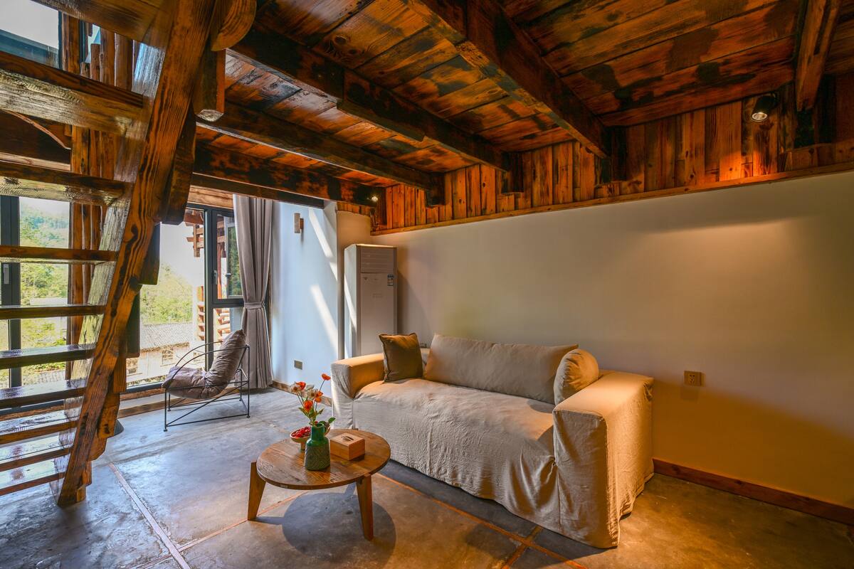 Een knus interieur met een houten plafond, een bank, een stoel en een klein tafeltje met een vaas.