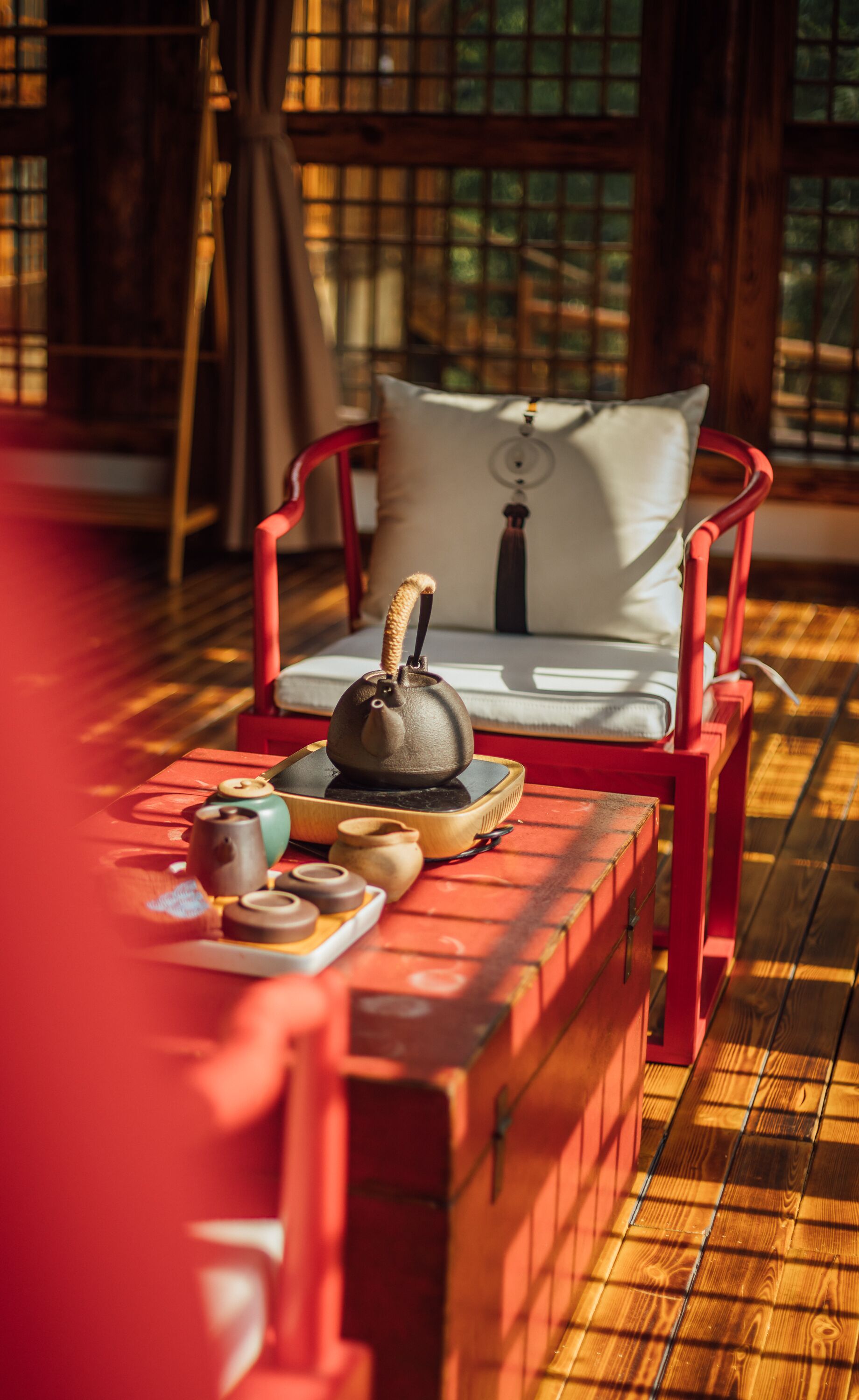 Une pièce chaleureuse avec un fauteuil rouge, une table sur laquelle se trouvent une théière, des tasses et un plateau.