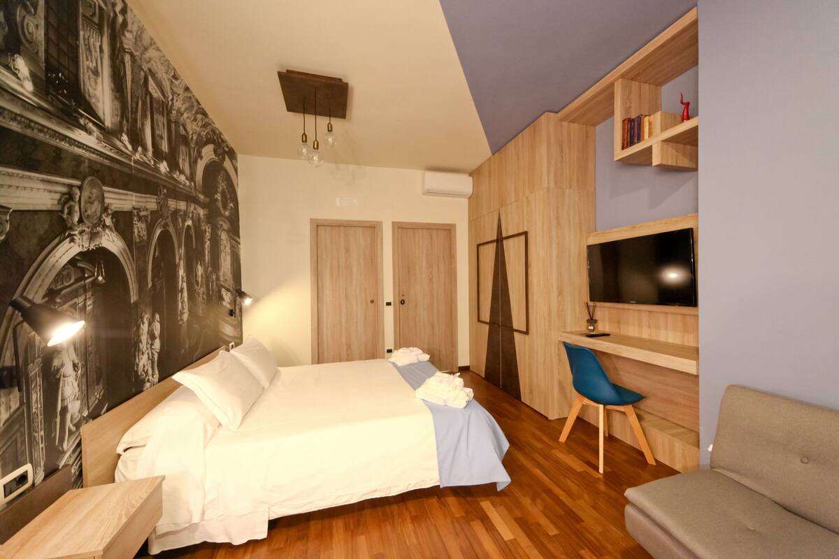 A bedroom with a bed, a desk, a chair, and a TV.