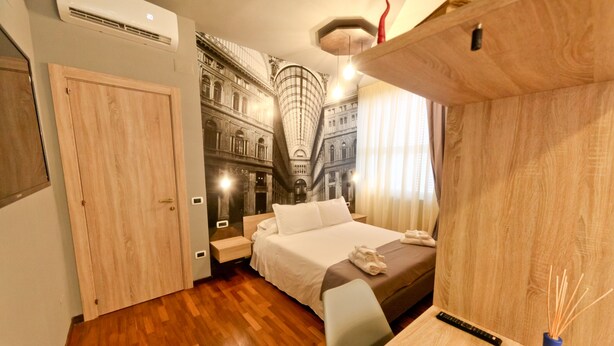 Habitación de hotel con cama, suelo de madera, un escritorio con un florero y un mural de un edificio en la pared.