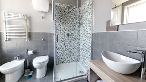 Un baño moderno con ducha de vidrio, un bidé, un inodoro y un lavabo grande tipo recipiente.