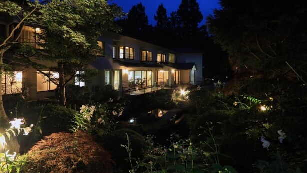 A two-story house with a covered patio and a pond in the garden.