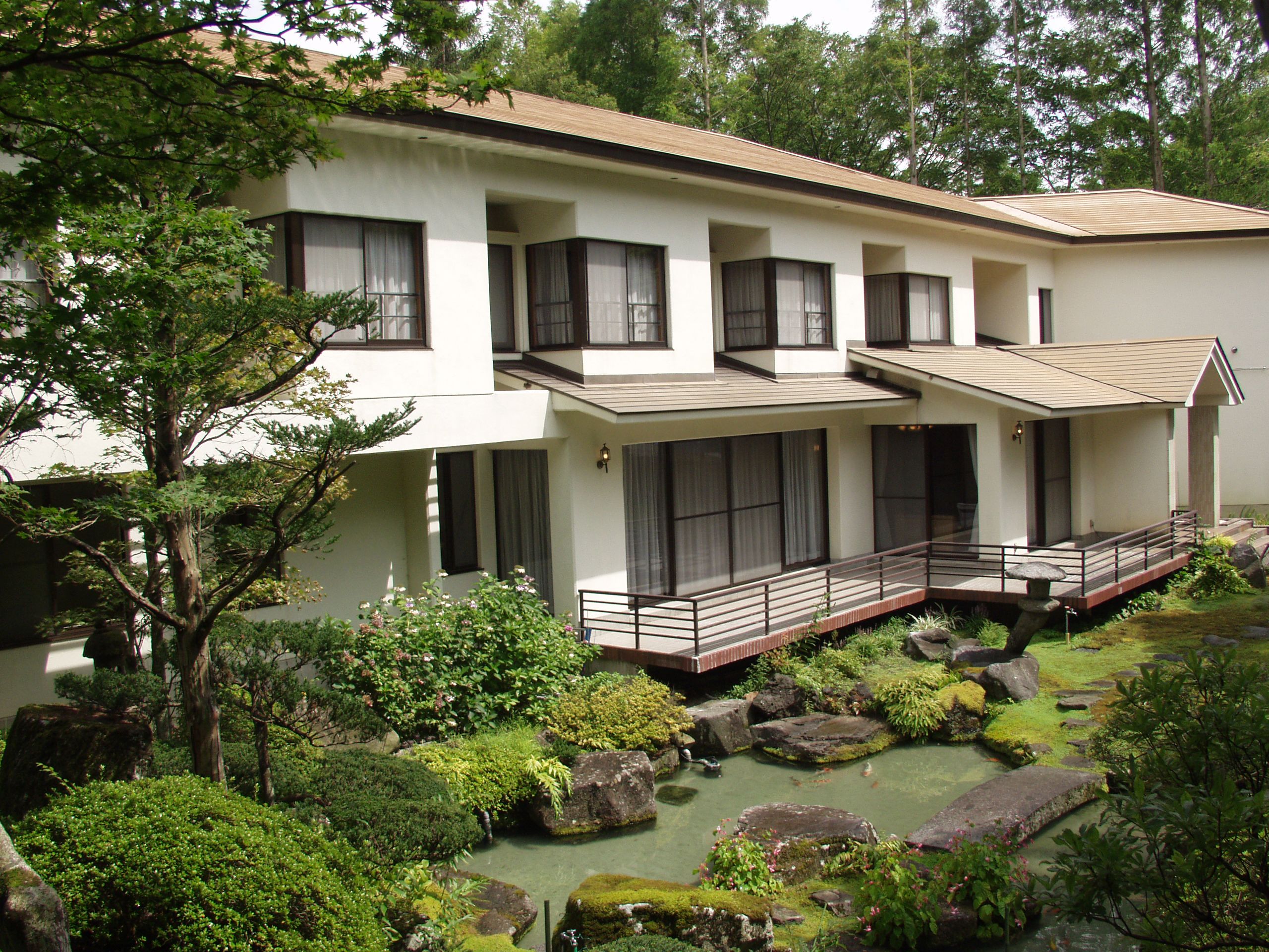 A modern two-story building with a covered outdoor area and a small pond with rocks and plants.