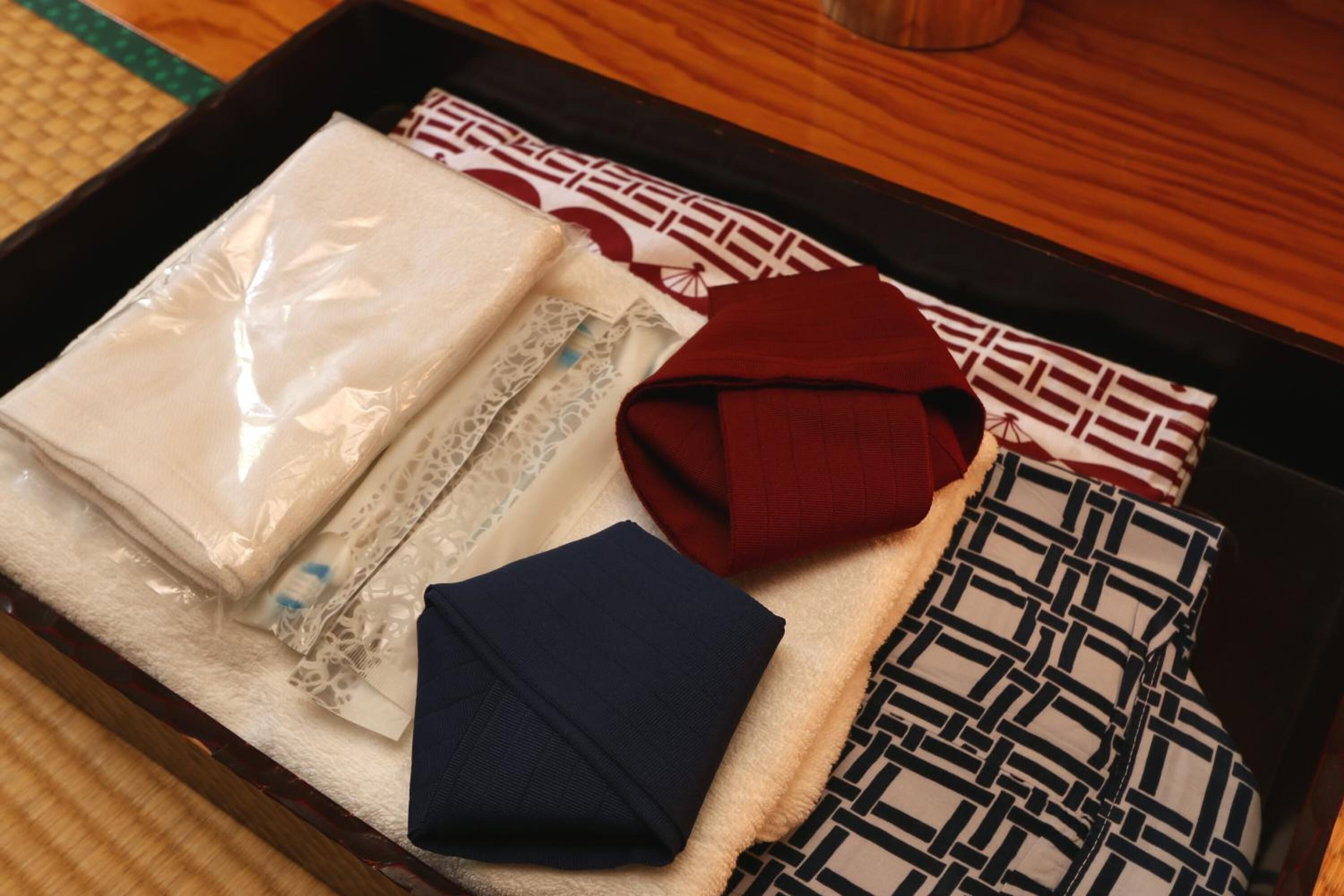 A neatly arranged tray with various textiles, including a folded white fabric, a red garment, a blue piece of clothing, and patterned cushions.