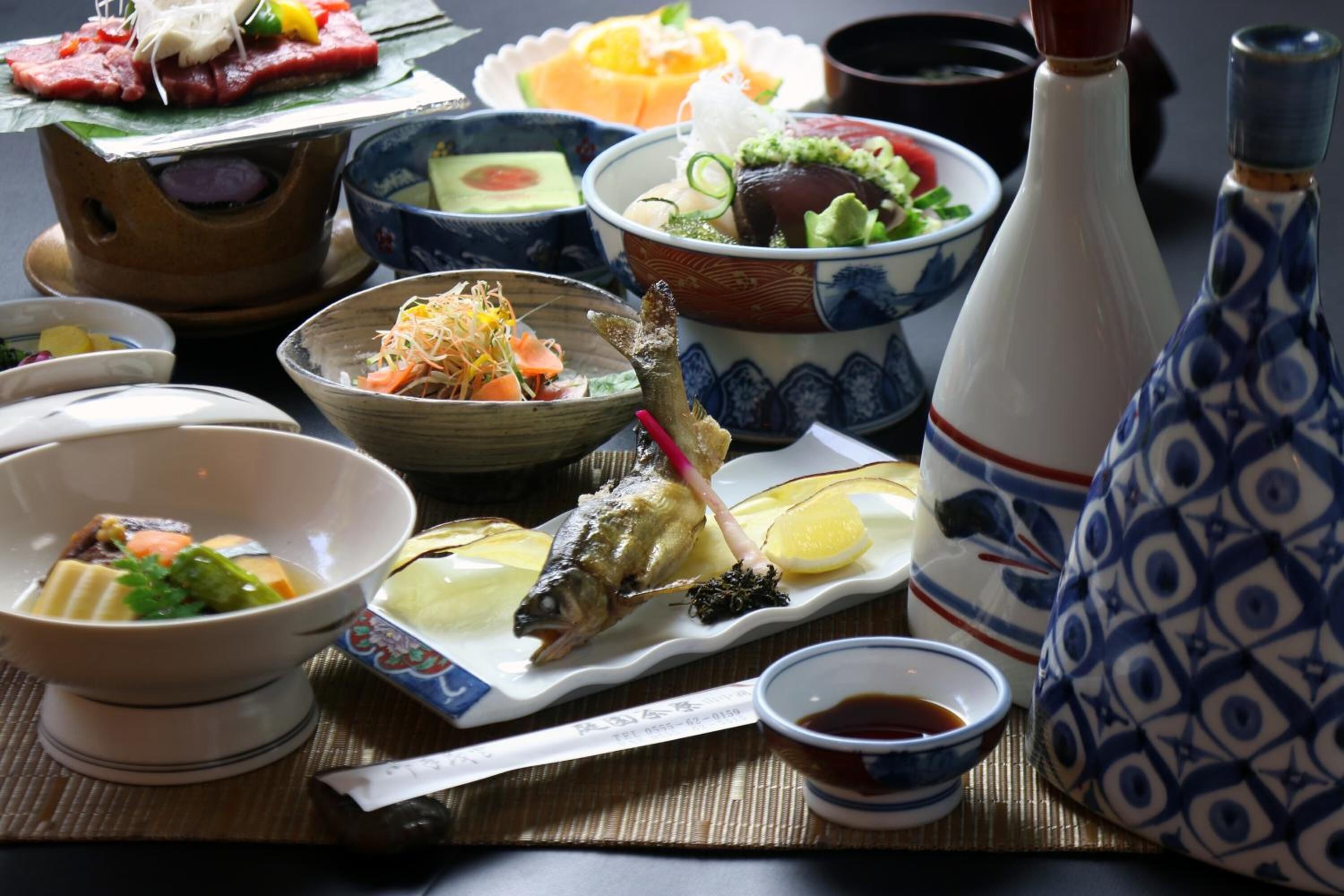 A variety of dishes including fish, vegetables, and possibly meat, served on traditional Japanese bowls and plates.