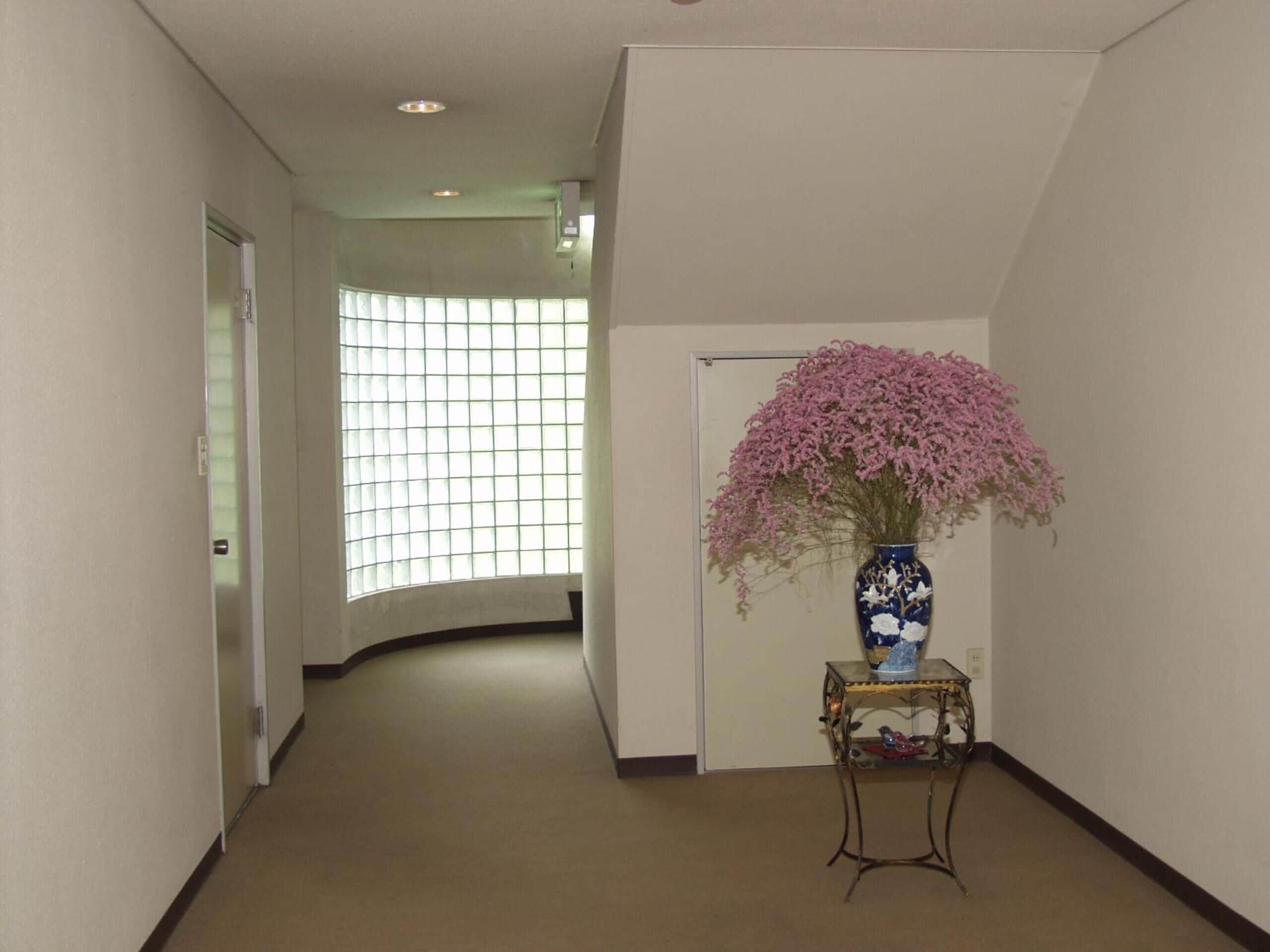 A hallway with a curved ceiling, a window with a grid pattern, and a vase with pink flowers on a small table.