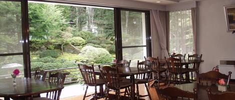 A dining area with large windows, wooden tables, and chairs.