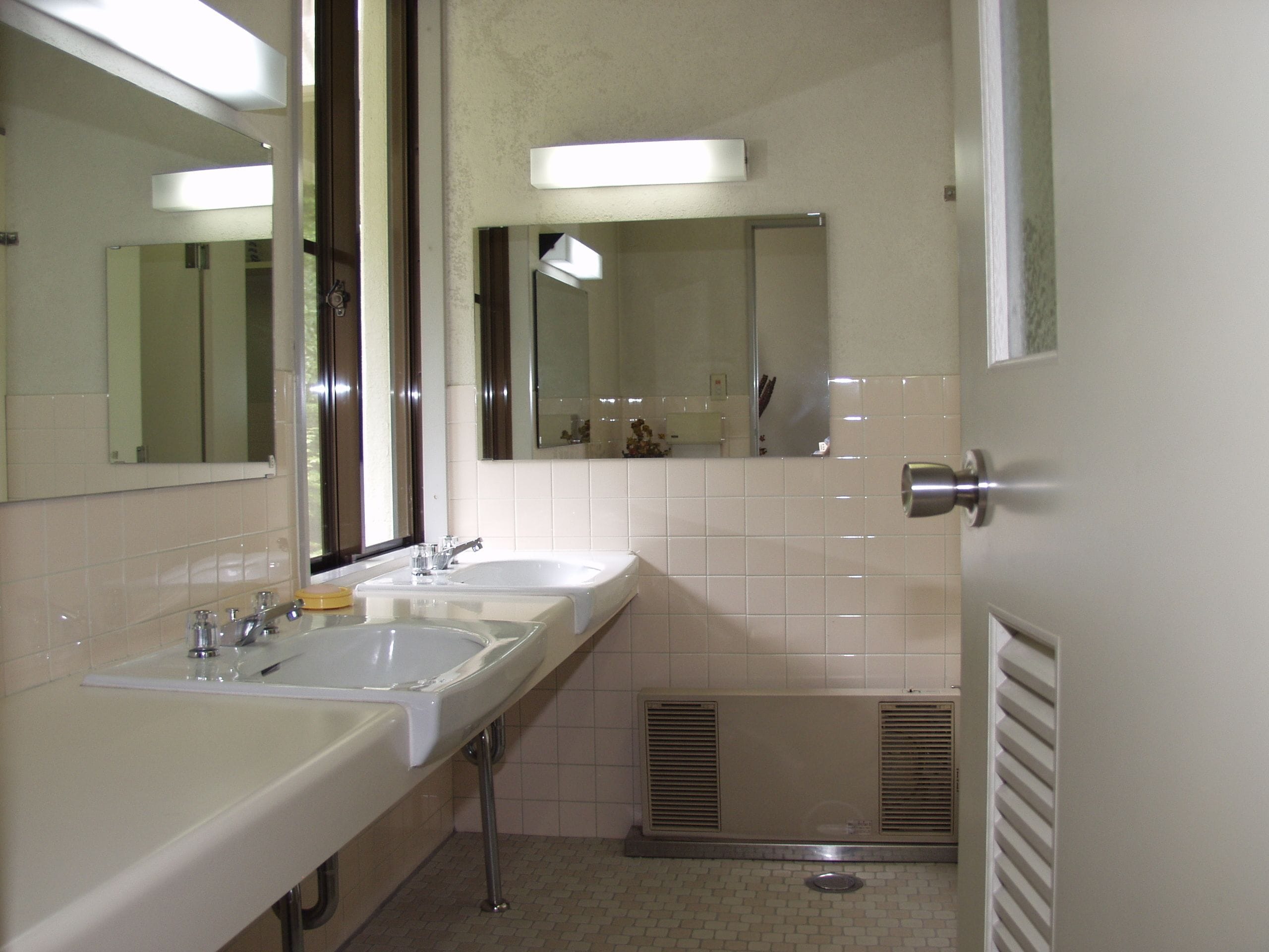 A bathroom with two sinks, a mirror, and a ventilation system.