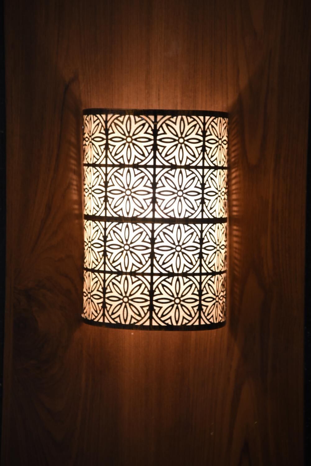 Un luminaire de forme carrée, doté d’un design complexe et d’un motif géométrique, fixé sur une surface en bois.