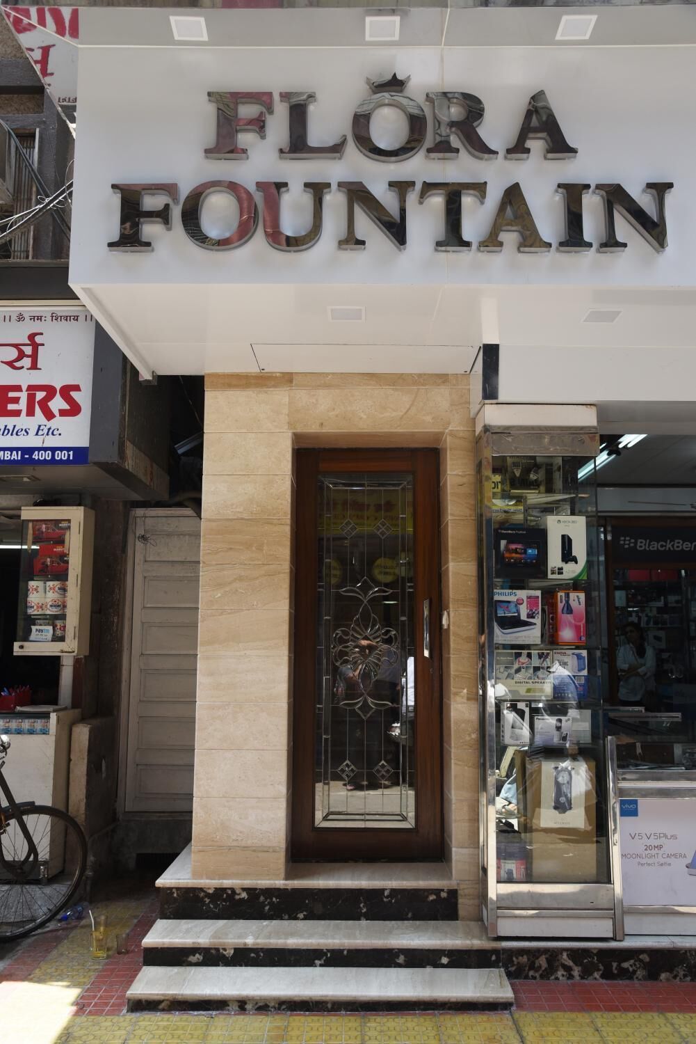 De buitenkant van Flora Fountain, met een opvallend bord en een glazen ingang.