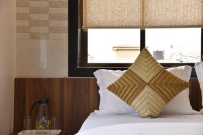 Hotelkamer met een bed, een raam met uitzicht op gebouwen, een houten hoofdbord en een nachtkastje met een glazen pot en een groene fles.