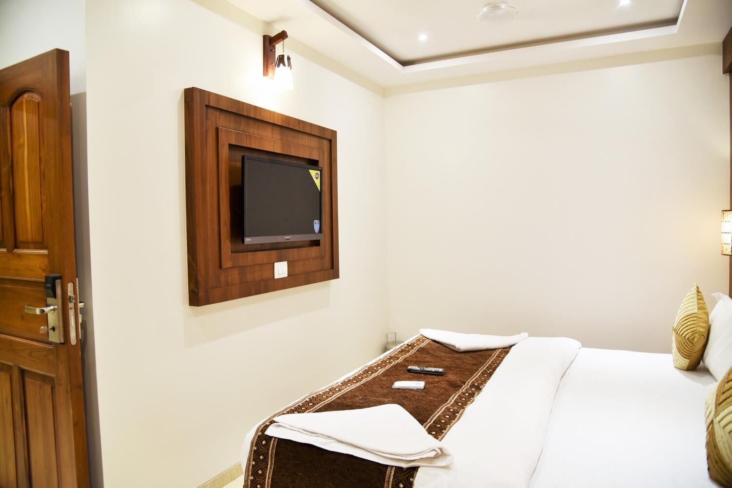 A hotel room with a bed, a TV mounted on the wall, a bedside table, and a door.