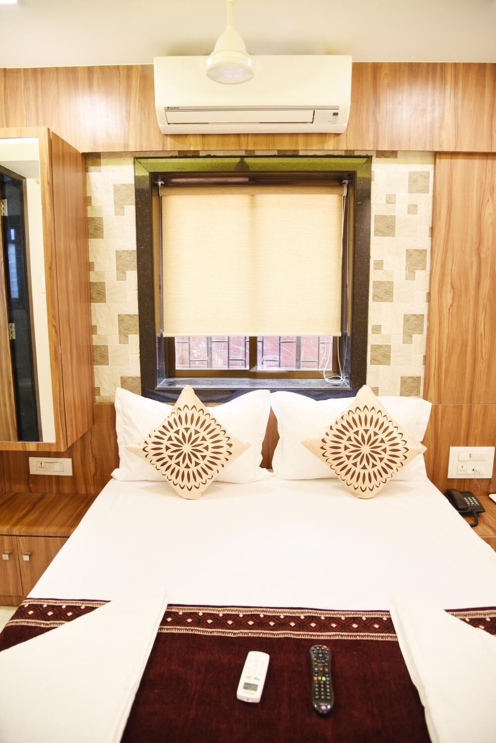 A hotel room with a bed, two decorative pillows, a remote control, and a telephone on the nightstand.