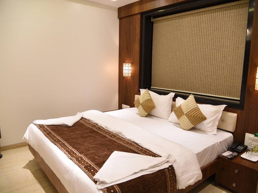 Cama bem arrumada com manta estampada, duas luminárias de cabeceira e mesa de cabeceira com telefone e copo.