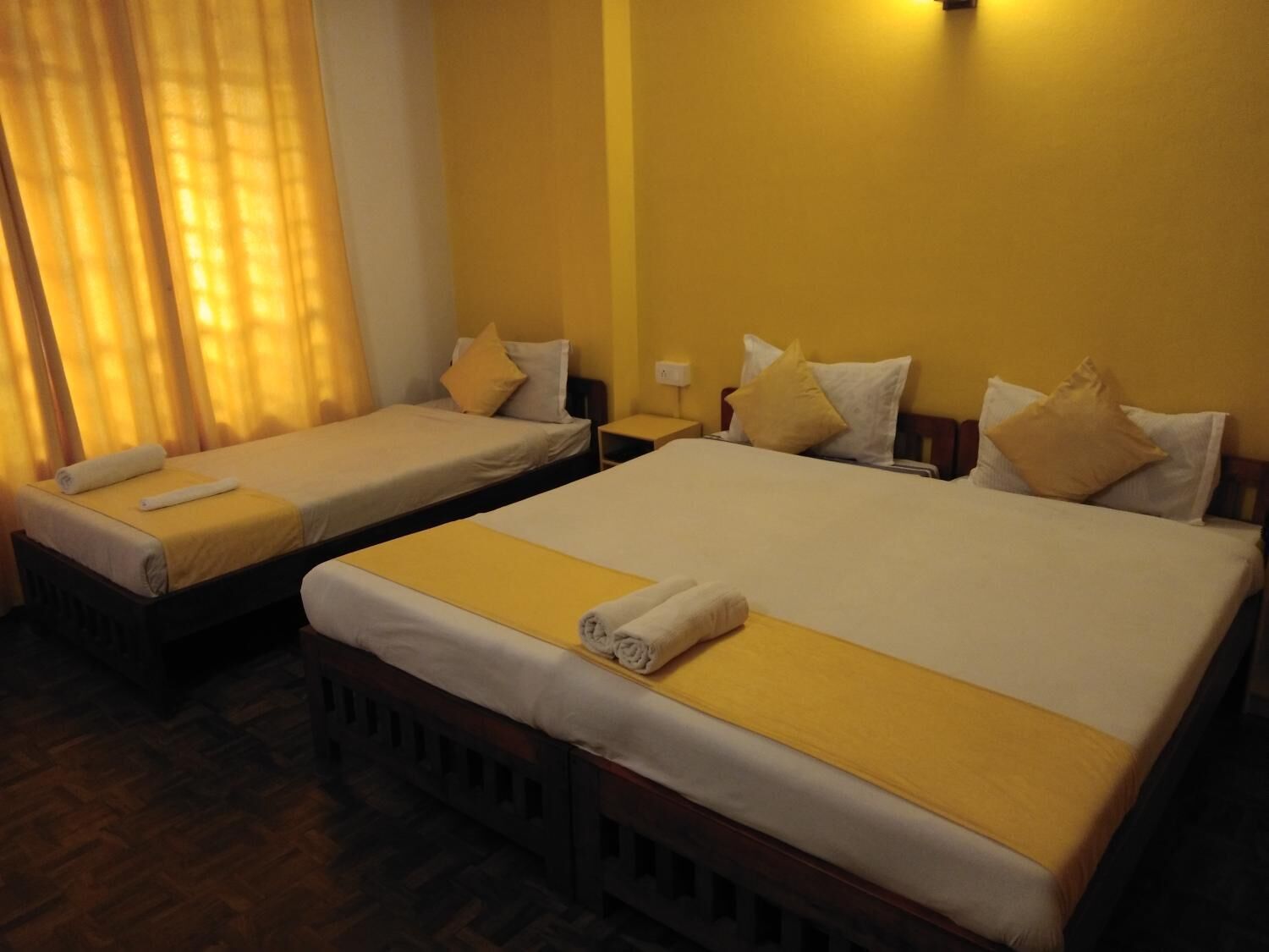 Ein Hotelzimmer mit zwei Einzelbetten und einem Doppelbett, jeweils mit gelber Bettdecke und Kissen.