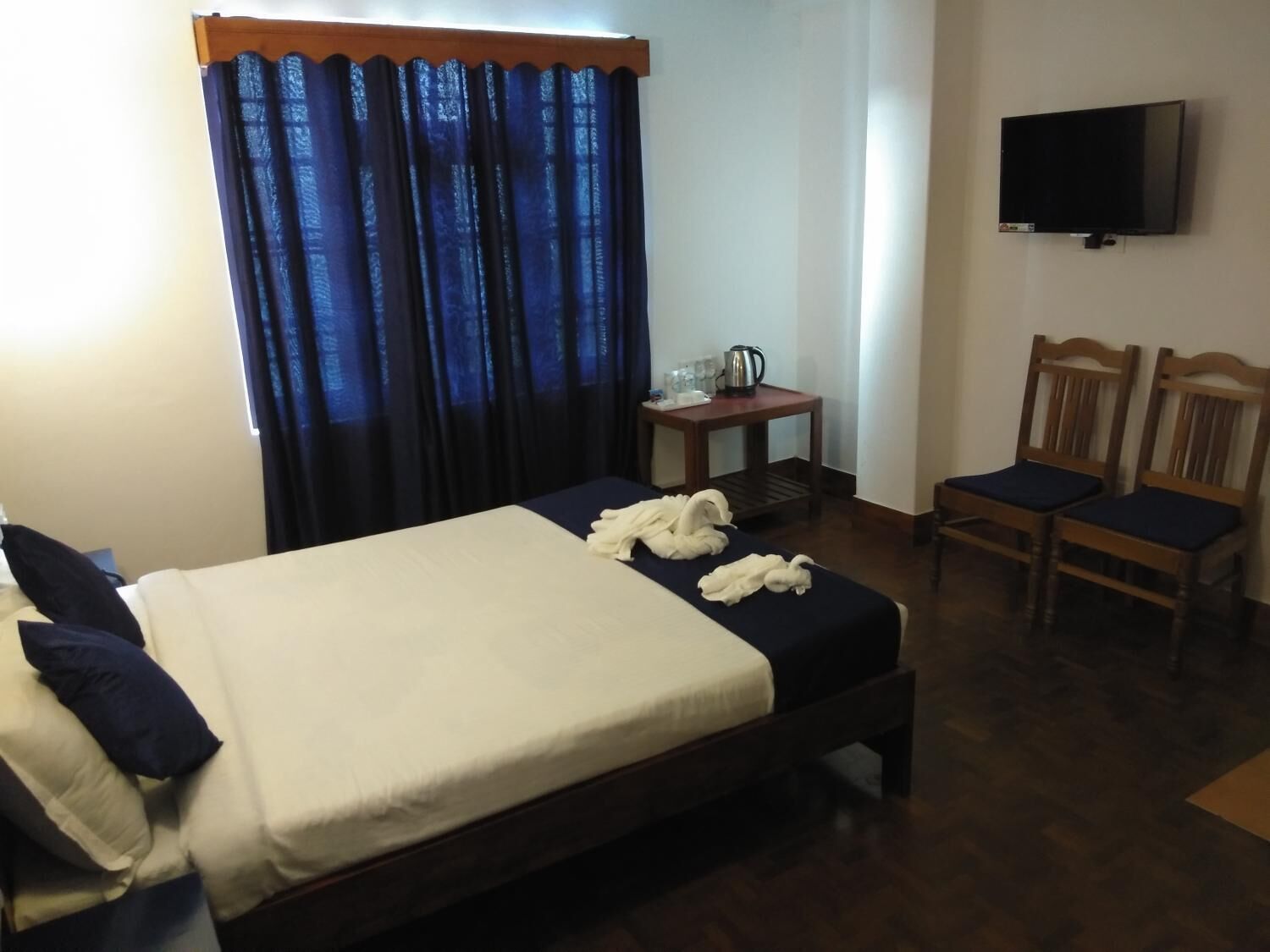 A hotel room with a bed, a TV mounted on the wall, and two wooden chairs.
