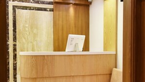 Zona de recepción con un escritorio de madera, una computadora portátil y un banco acolchado.