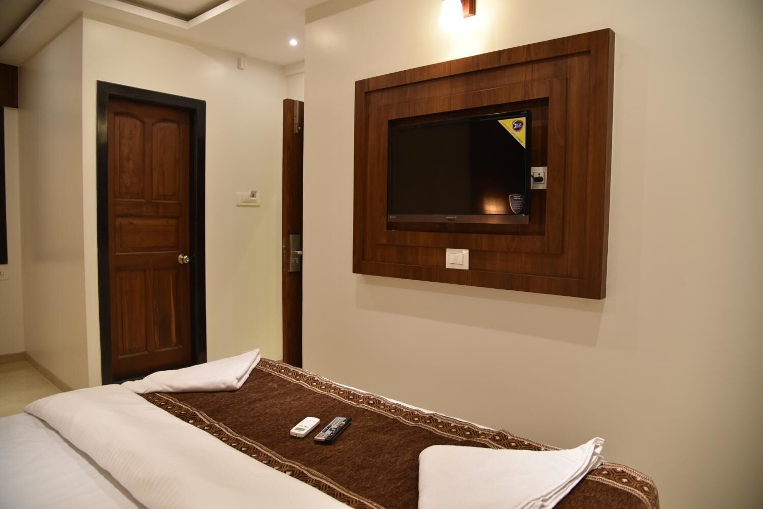 Une chambre d’hôtel avec un lit, un téléviseur fixé au mur et une porte en bois.