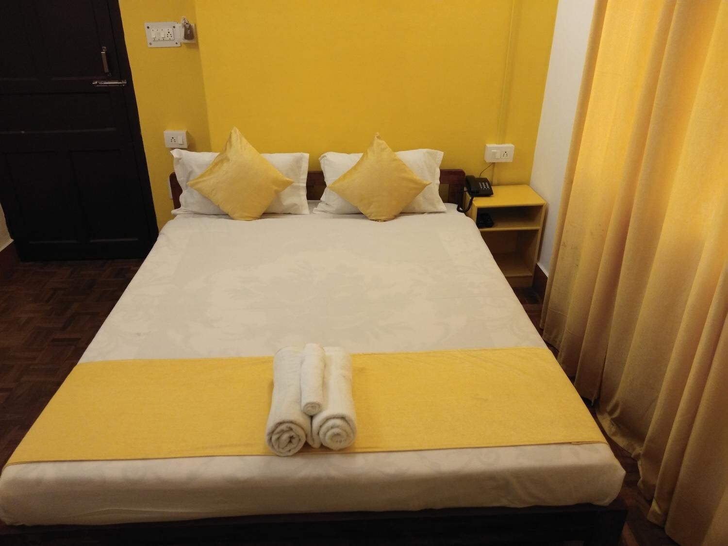 Ein Hotelzimmer mit Bett, gelben Kissen, einem Nachttisch mit Telefon und einer gelben Bettdecke.