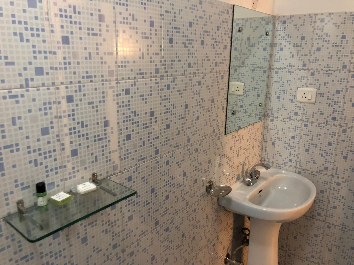 A bathroom with mosaic tile walls, a glass shelf with toiletries, and a white sink.