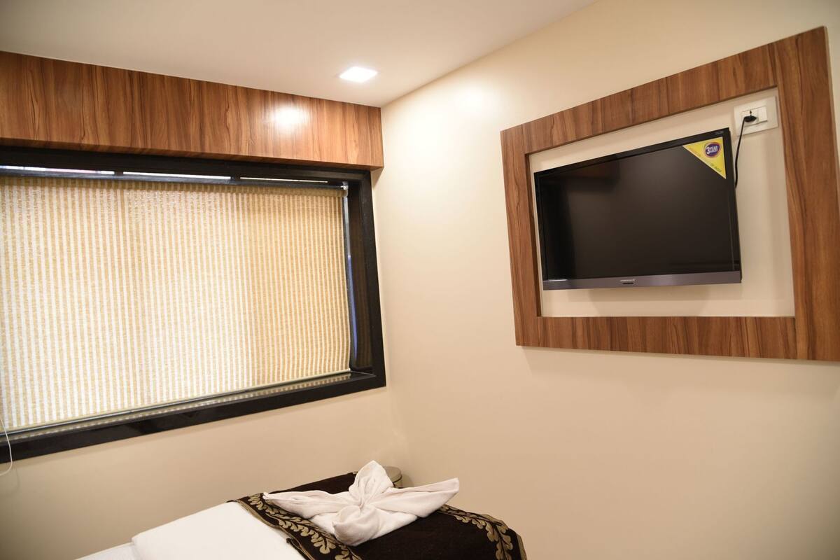 A hotel room with a window, a television mounted on the wall, and a bed with a towel.