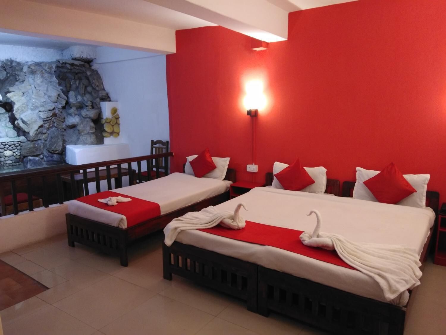 A hotel room with two single beds, a large bed, and a stone wall feature.