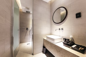 A modern bathroom with a glass shower enclosure, a round mirror, and a countertop with a sink and toiletries.