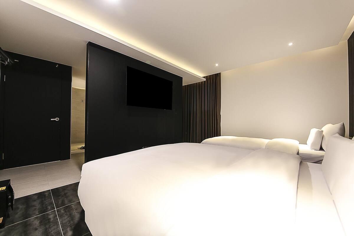 A modern hotel room with a large bed, a flat-screen TV mounted on the wall, and a dark-colored wardrobe.