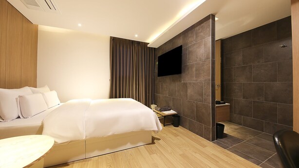 Una habitación de hotel moderna con una cama, mesita de noche y televisor montado en la pared.