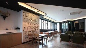Una cafetería moderna con una barra larga, mesas y sillas de madera, y una pared con ilustraciones sobre café.