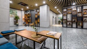 A modern lobby with a wooden reception desk, seating area, and decorative shelves. - Hotel With Jeju (Jeju City)
