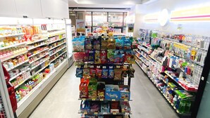 A brightly lit grocery store aisle with shelves stocked with snacks, beverages, and household items. - Hotel With Jeju (Jeju City)