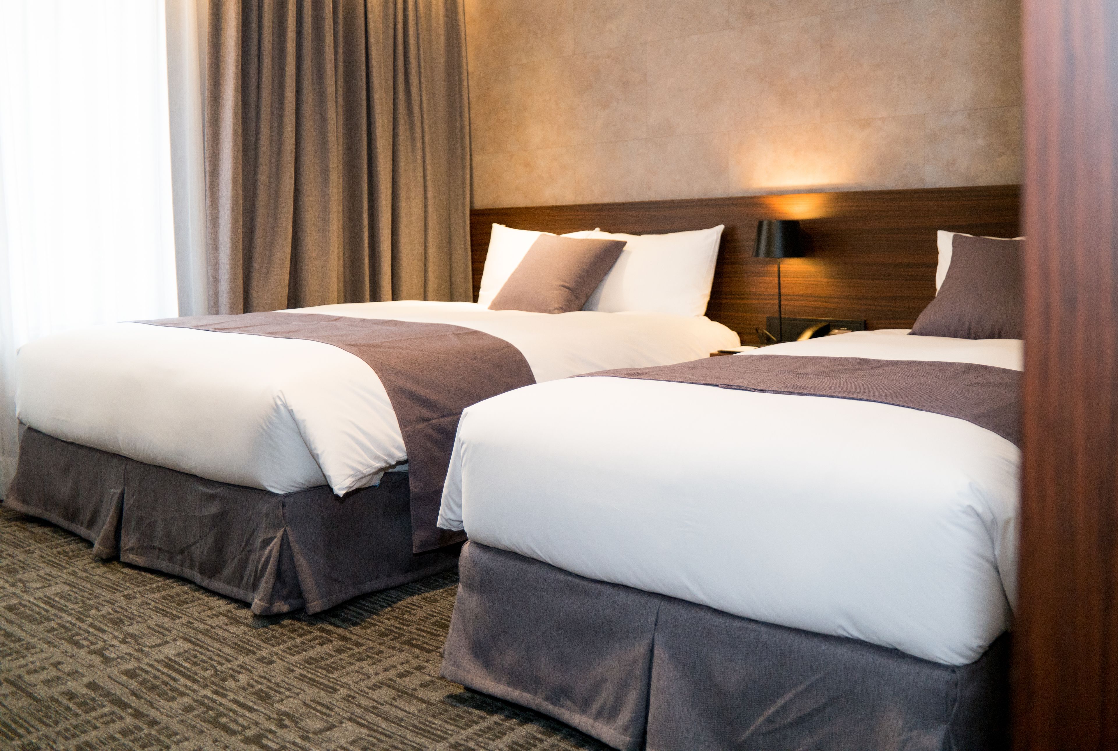 Ein Hotelzimmer mit zwei Betten, einem Kopfteil mit Lampenaufsatz und Teppichboden.