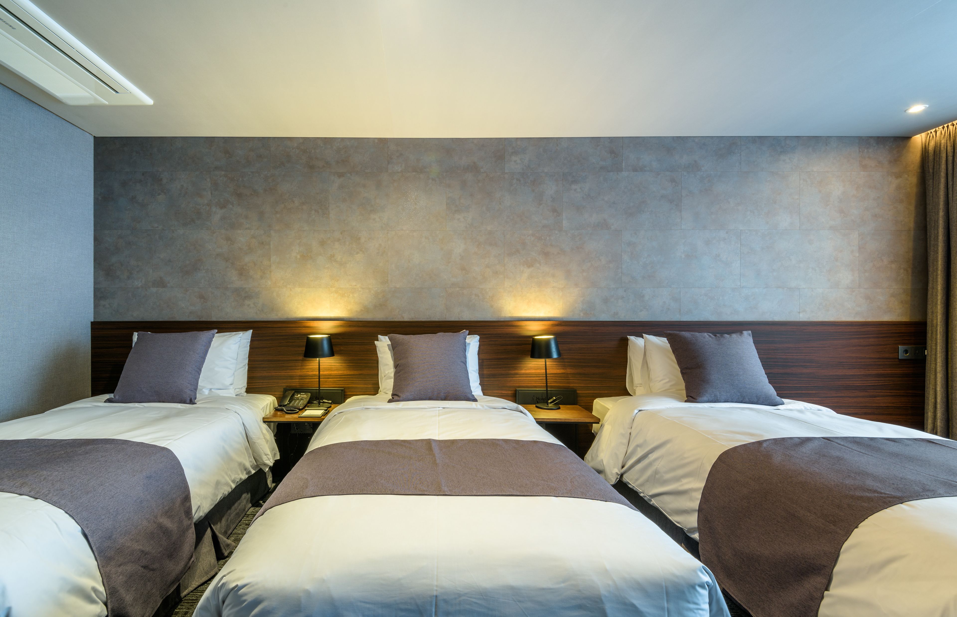 A hotel room with three beds, a wooden headboard, bedside lamps, and a telephone on the nightstand.