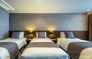Habitación de hotel con tres camas, cabecero de madera, lámparas de noche y un teléfono en la mesita de noche.