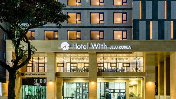 A hotel with a modern facade, multiple floors, and a prominent entrance with glass doors. - Hotel With Jeju (Jeju City)