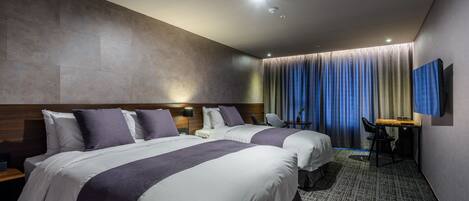 A hotel room with two beds, a desk, a chair, a TV, and a large window with curtains.