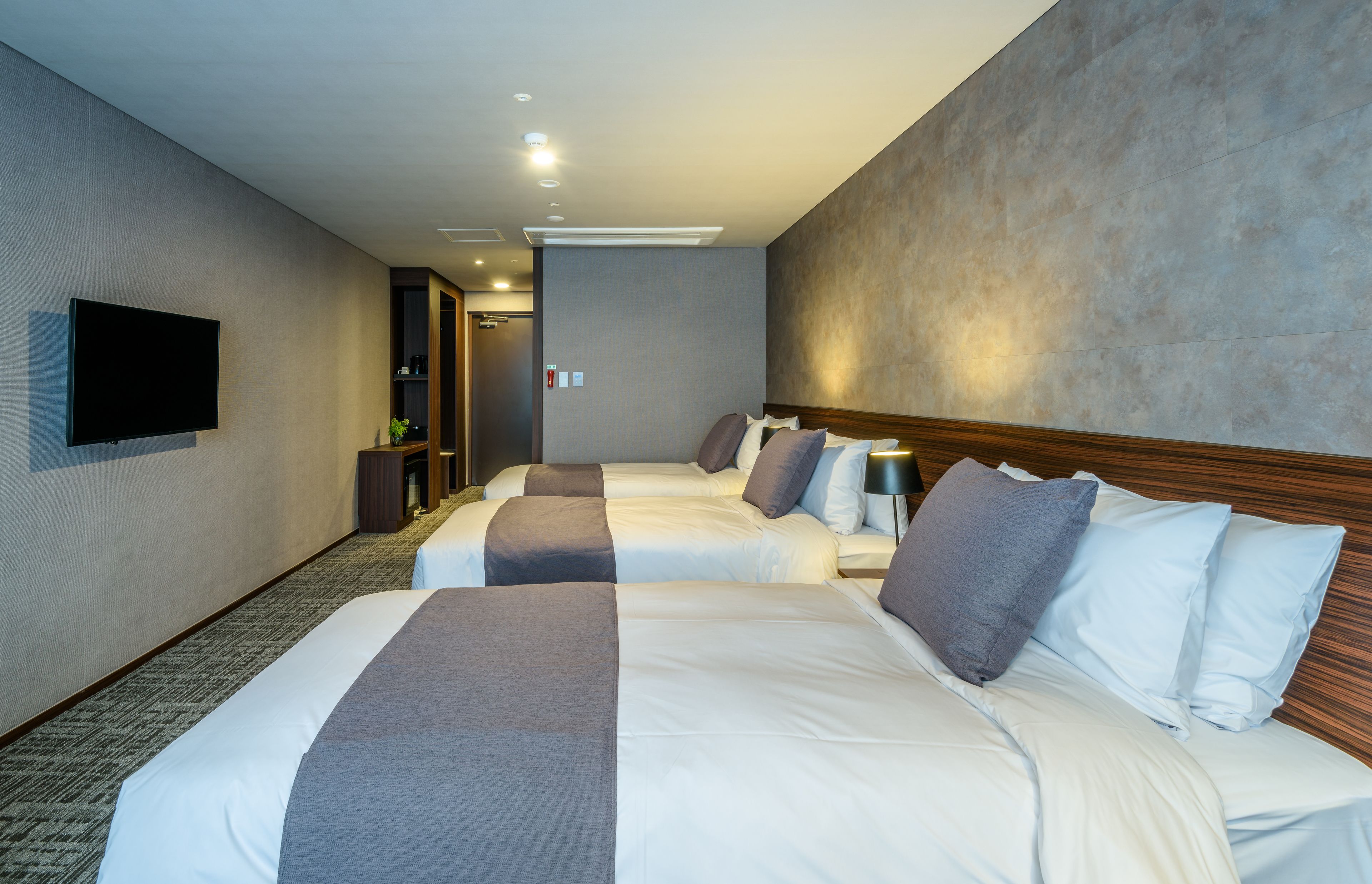 A hotel room with three beds, a flat-screen TV mounted on the wall, and a carpeted floor.