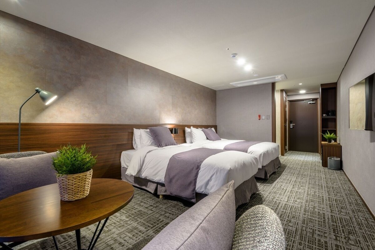Une chambre d’hôtel avec deux lits, un canapé, une petite table et une plante en pot.