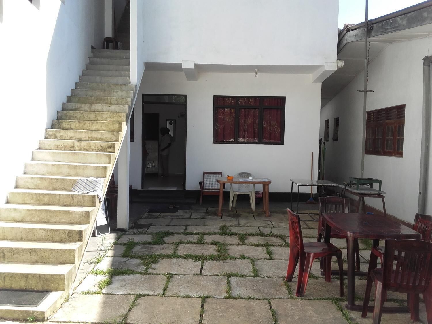 A staircase leading to a door, a small outdoor seating area with a table and chairs, and a window with red curtains.