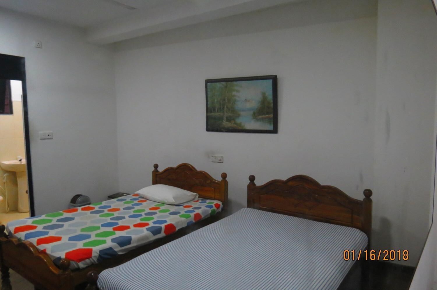 Una habitación pequeña y sencilla con dos camas individuales, un cabecero de madera, un cuadro en la pared y un lavamanos en una esquina.